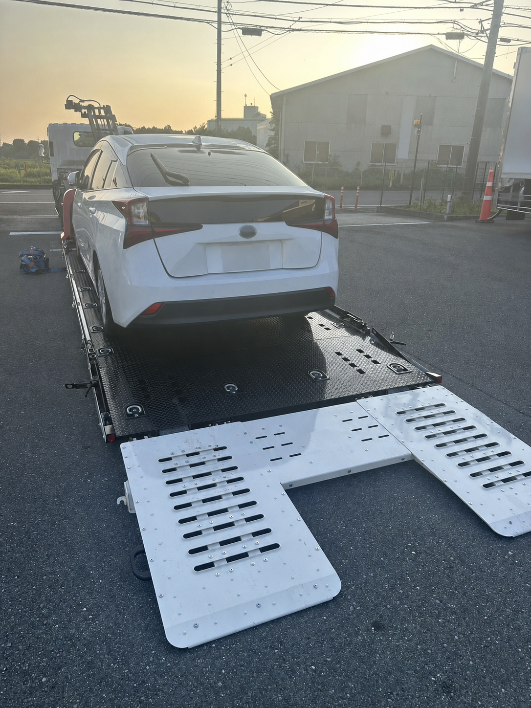 積載車（レッカー車）の荷台に載せられた白いプリウスを後方から写した写真