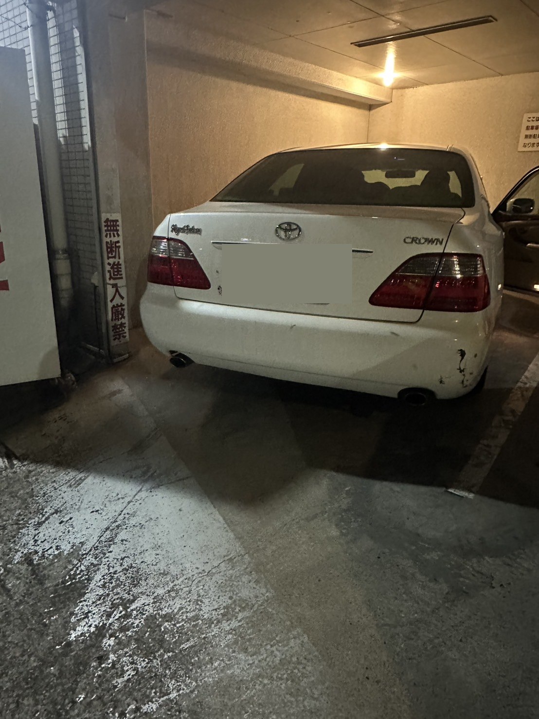 夜間の屋内駐車場に停まった白いセダンを後方から写した写真