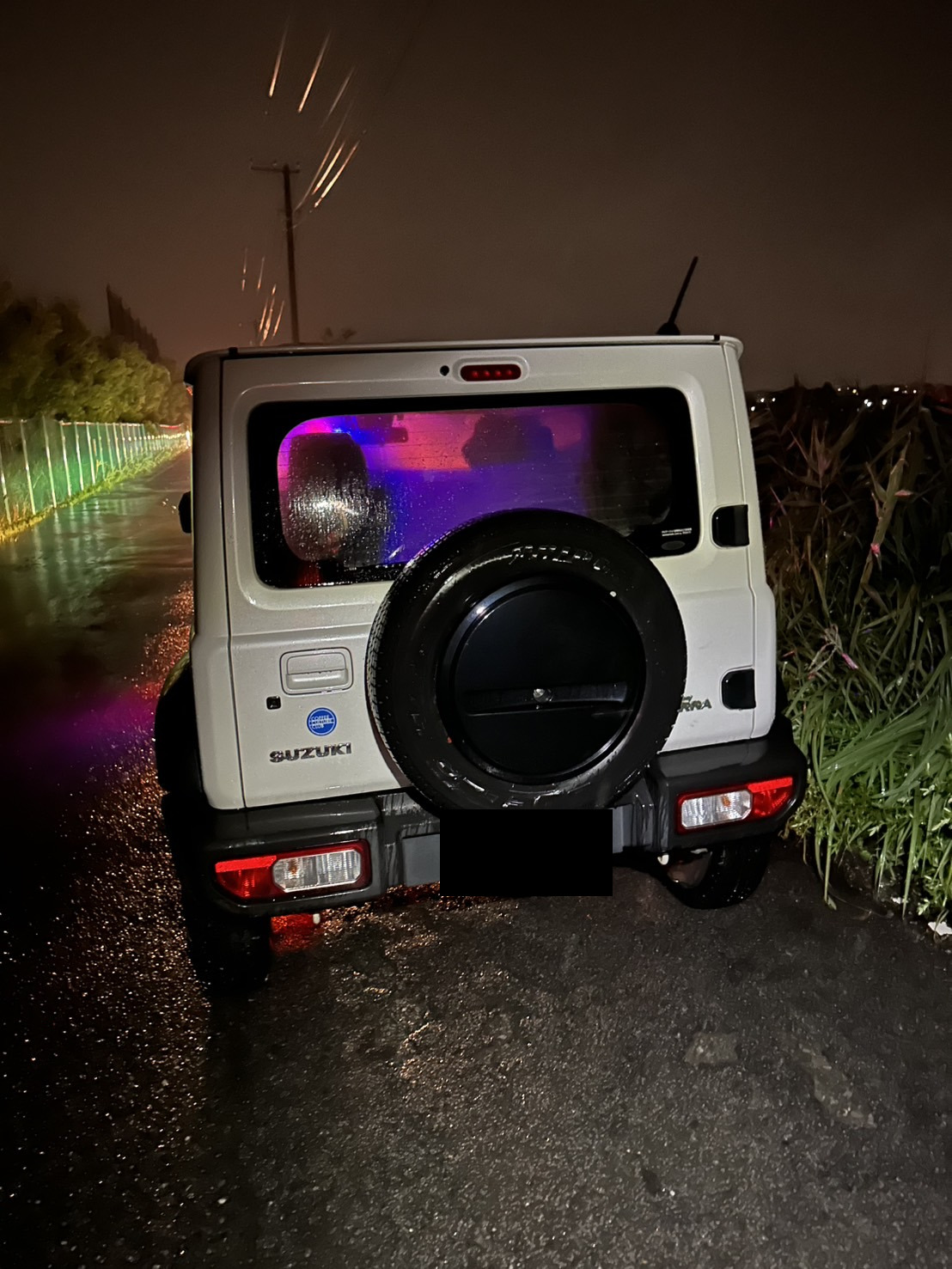 夜間の路上で作業車のライトに照らされた、脱輪した白いSUVの後部