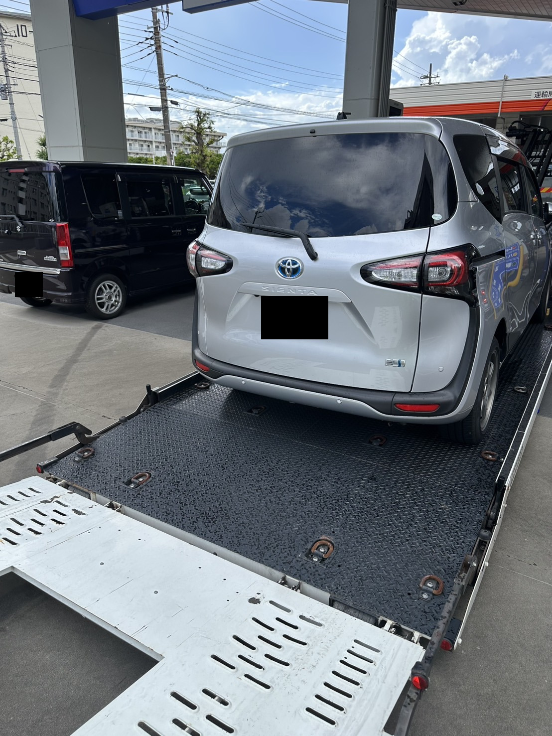 積載車の荷台に載せられたシルバーのミニバンを後方から見た様子