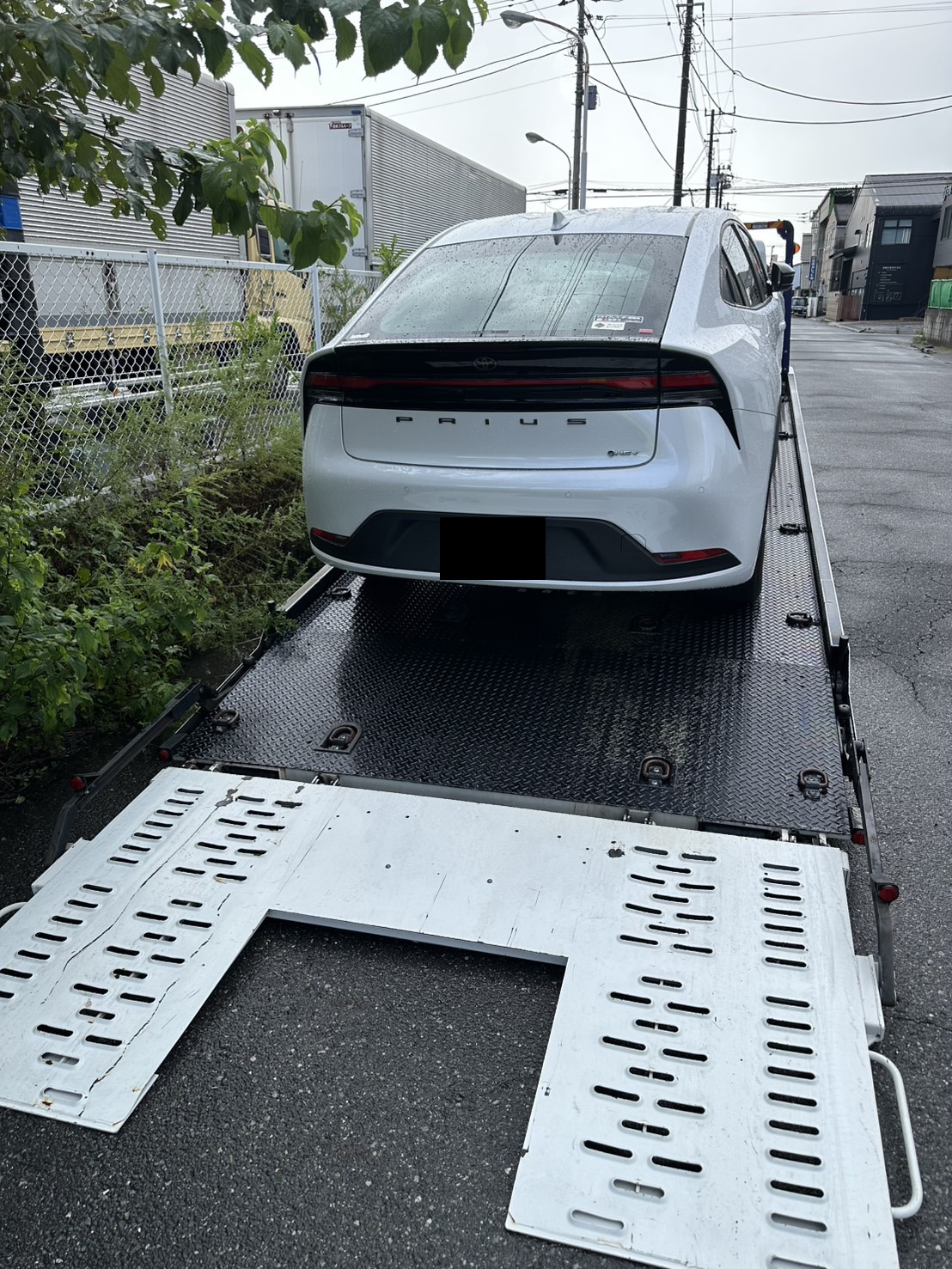 積載車の荷台に載せられた白いセダンを後方から見た様子