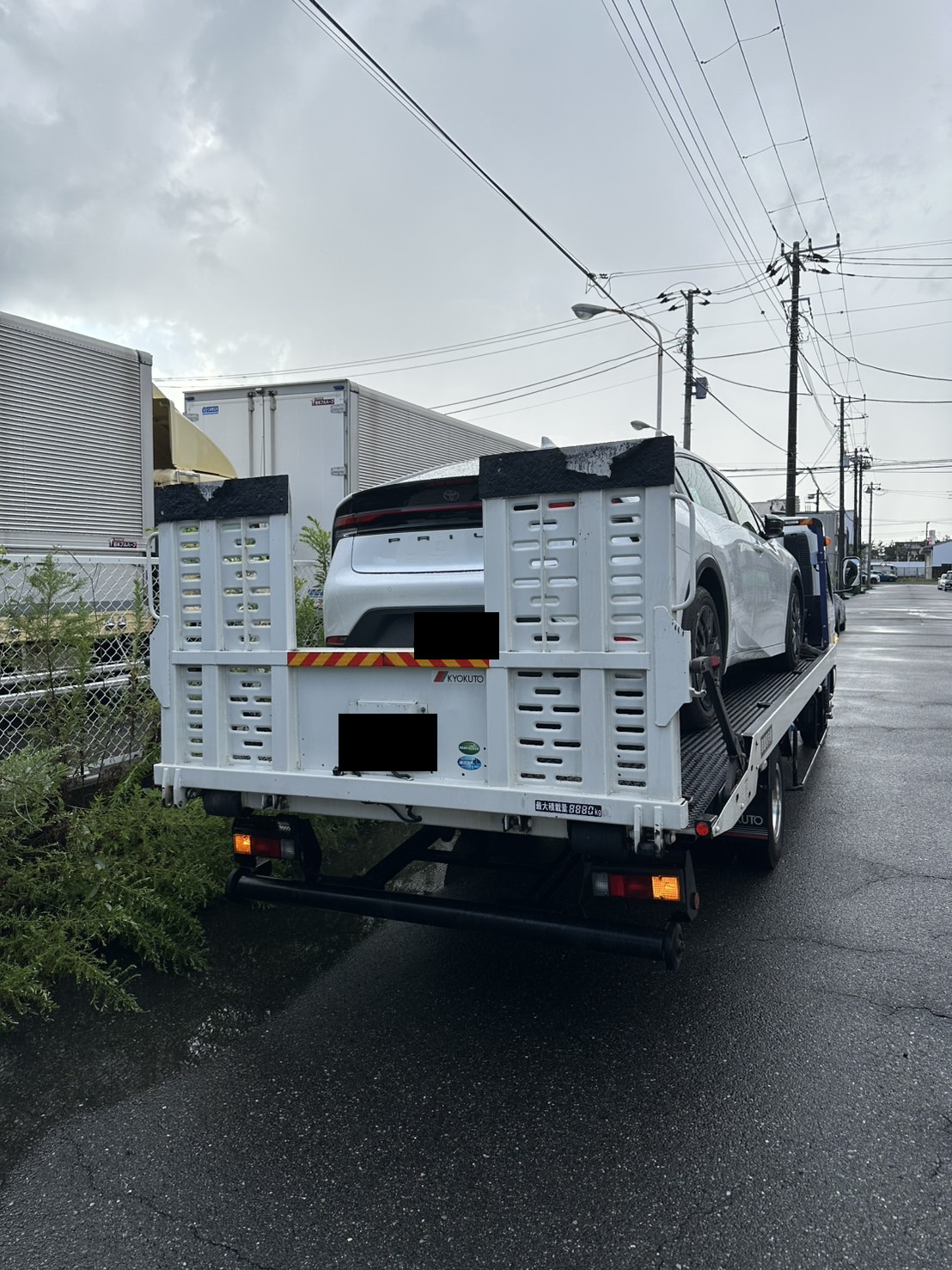 道路の後方から見た、白いセダンを積載した積載車