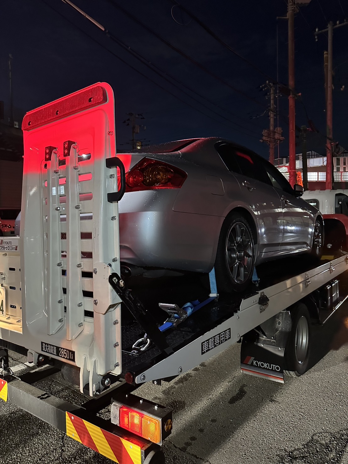 積載車の荷台に載せて固定されたシルバーのセダンを後方から見た様子
