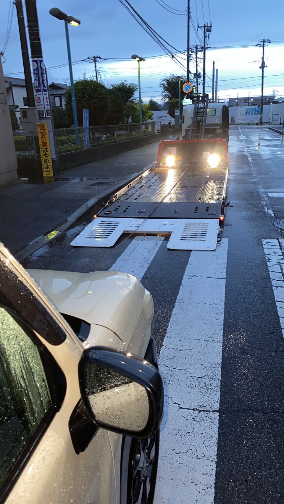 雨に濡れた路上で、積載車の荷台を下ろして作業の準備をしている様子