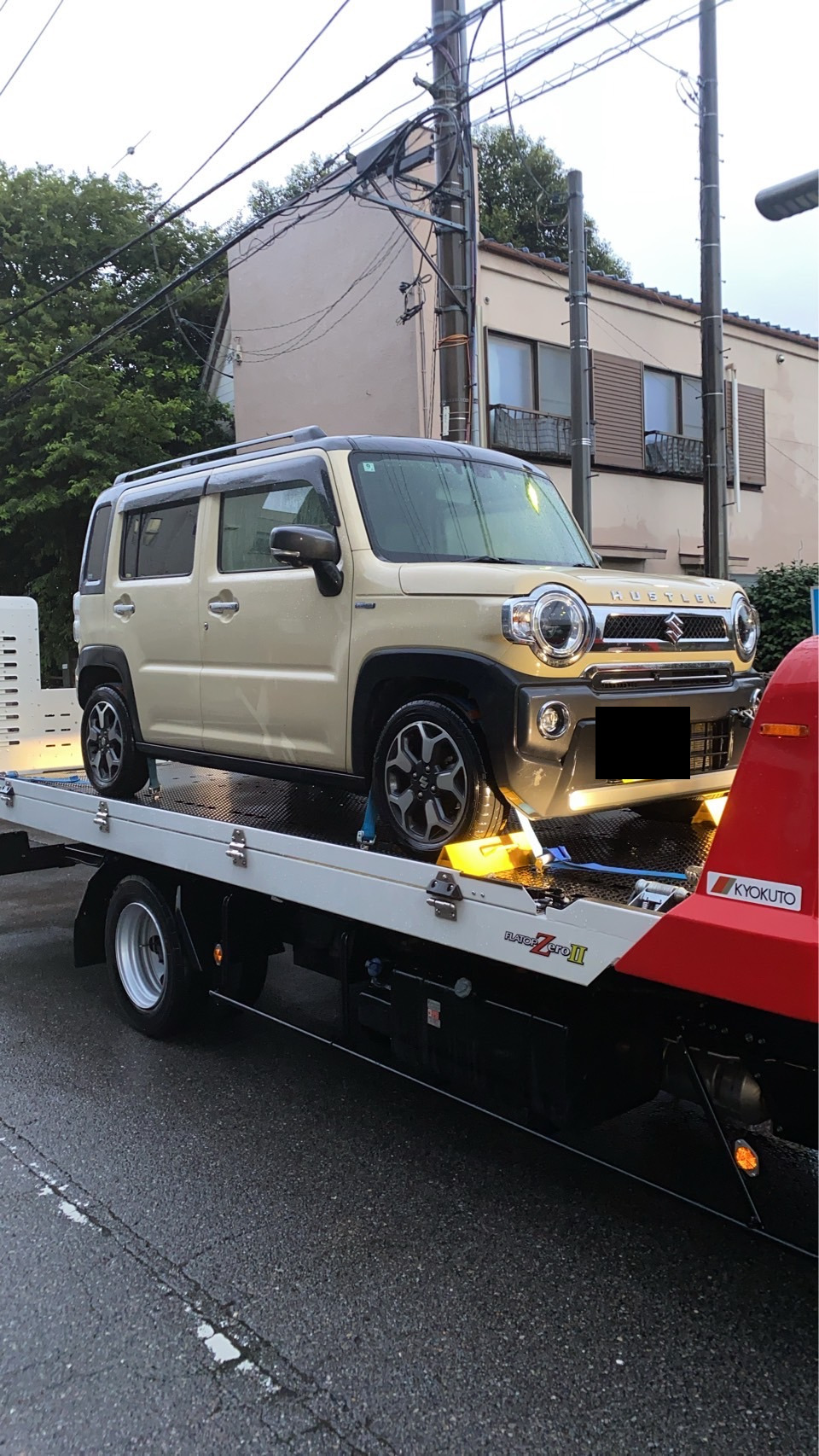 路上で積載車の荷台に載せられたベージュ色の軽自動車を正面から見た様子