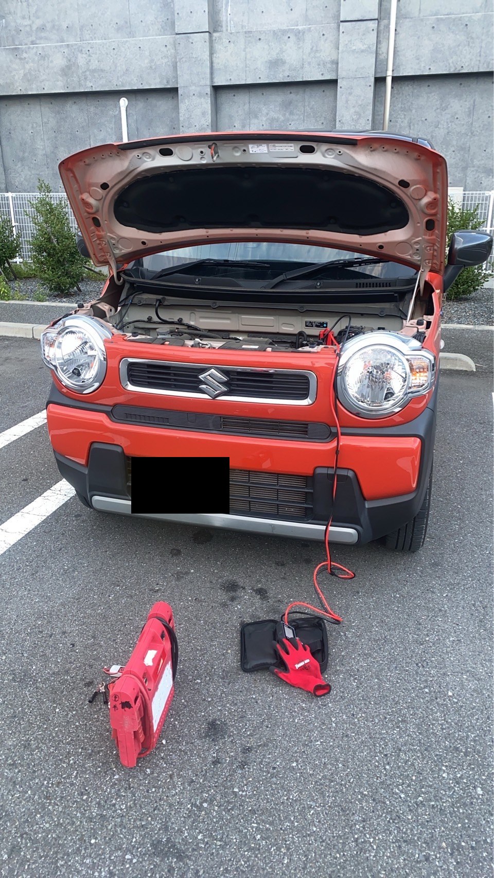 駐車場でボンネットを開け、ジャンプスターターをつないだ軽自動車（ナンバープレートはマスク処理）