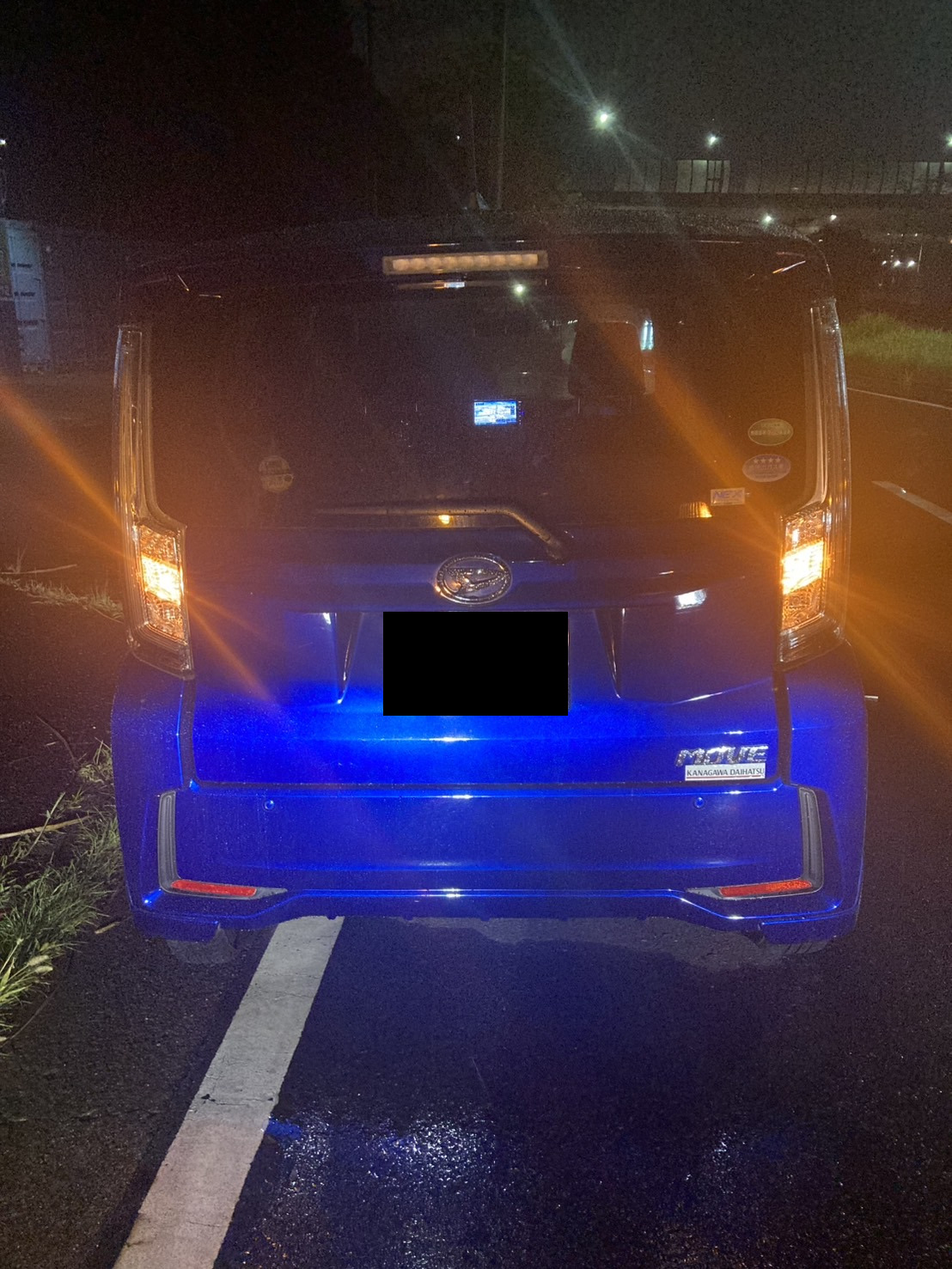 夜間の道路上に停車した青い軽自動車を後方から見た様子
