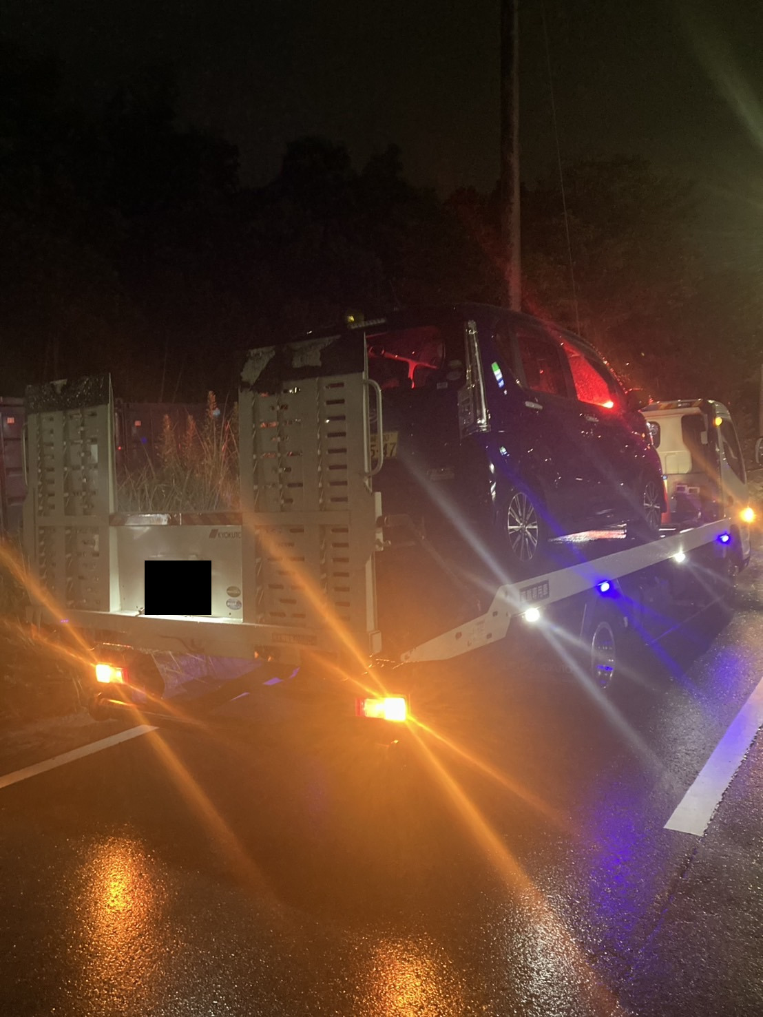 雨の夜、道路上で積載車へ軽自動車を積み込んでいる様子