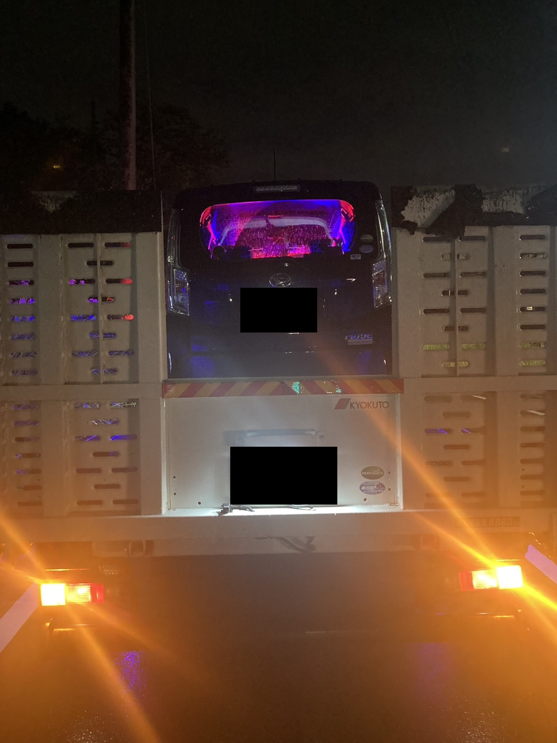 積載車の荷台に載せられた青い軽自動車を後方から見た様子