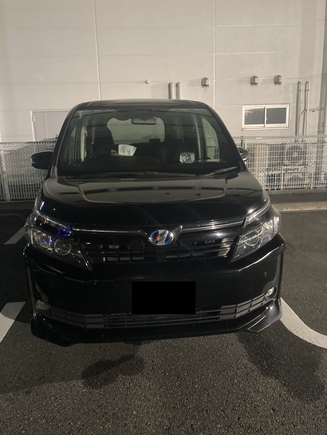 夜間、駐車場に停まった黒いミニバンを前方から見た様子（ナンバープレートはマスク処理）