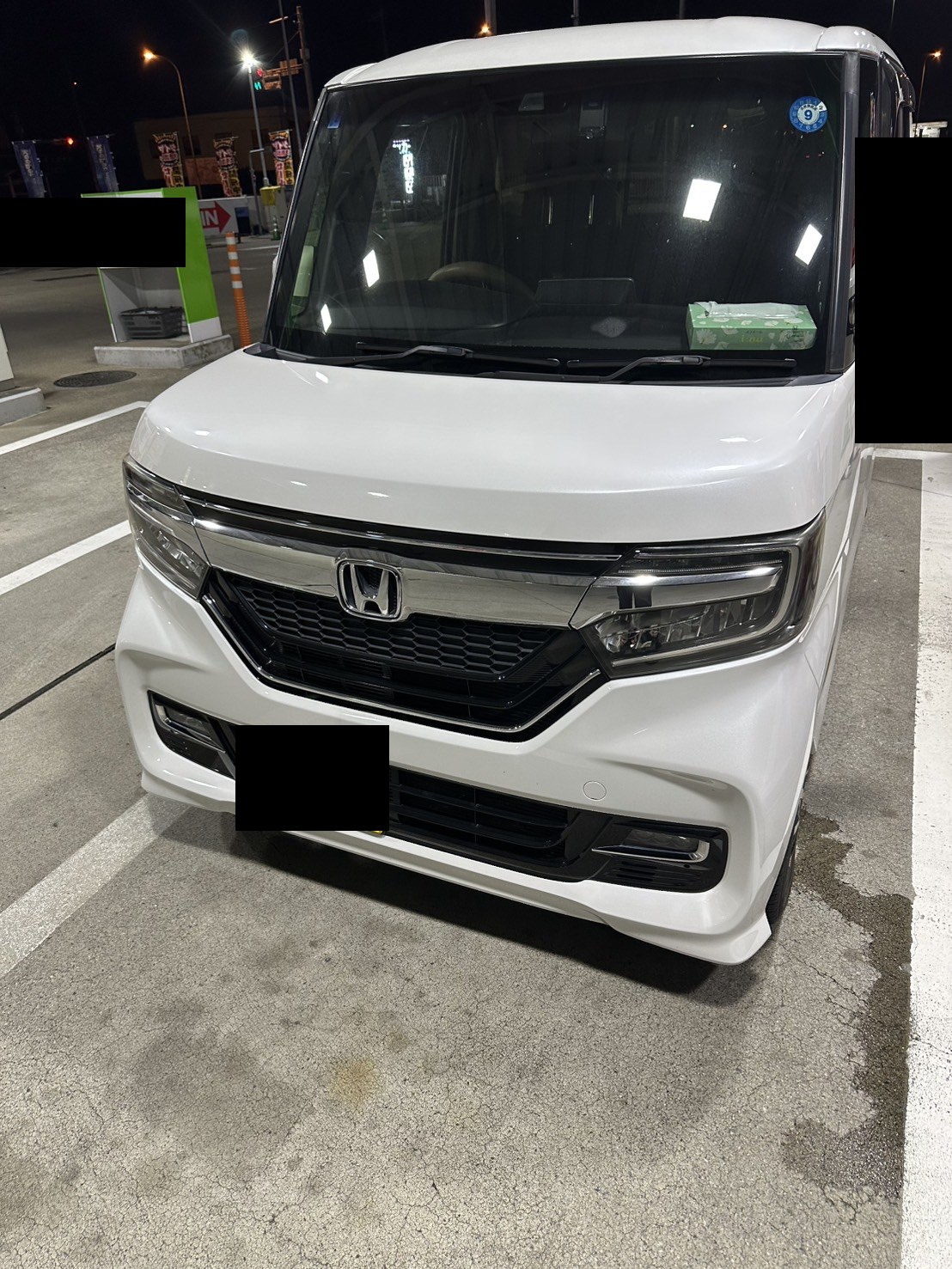 夜間、駐車場に停まった白い軽ワゴンを前方から見た様子（ナンバープレートはマスク処理）