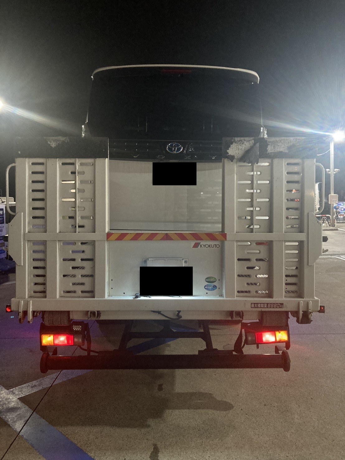 積載車の荷台に固定された白いミニバンを後方から見た様子（ナンバープレートはマスク処理）