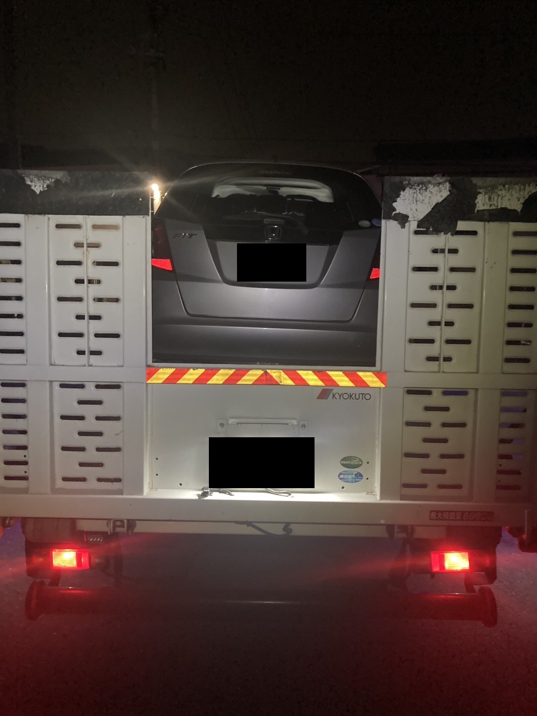 積載車の荷台に固定されたコンパクトカーを後方から見た様子（ナンバープレートはマスク処理）