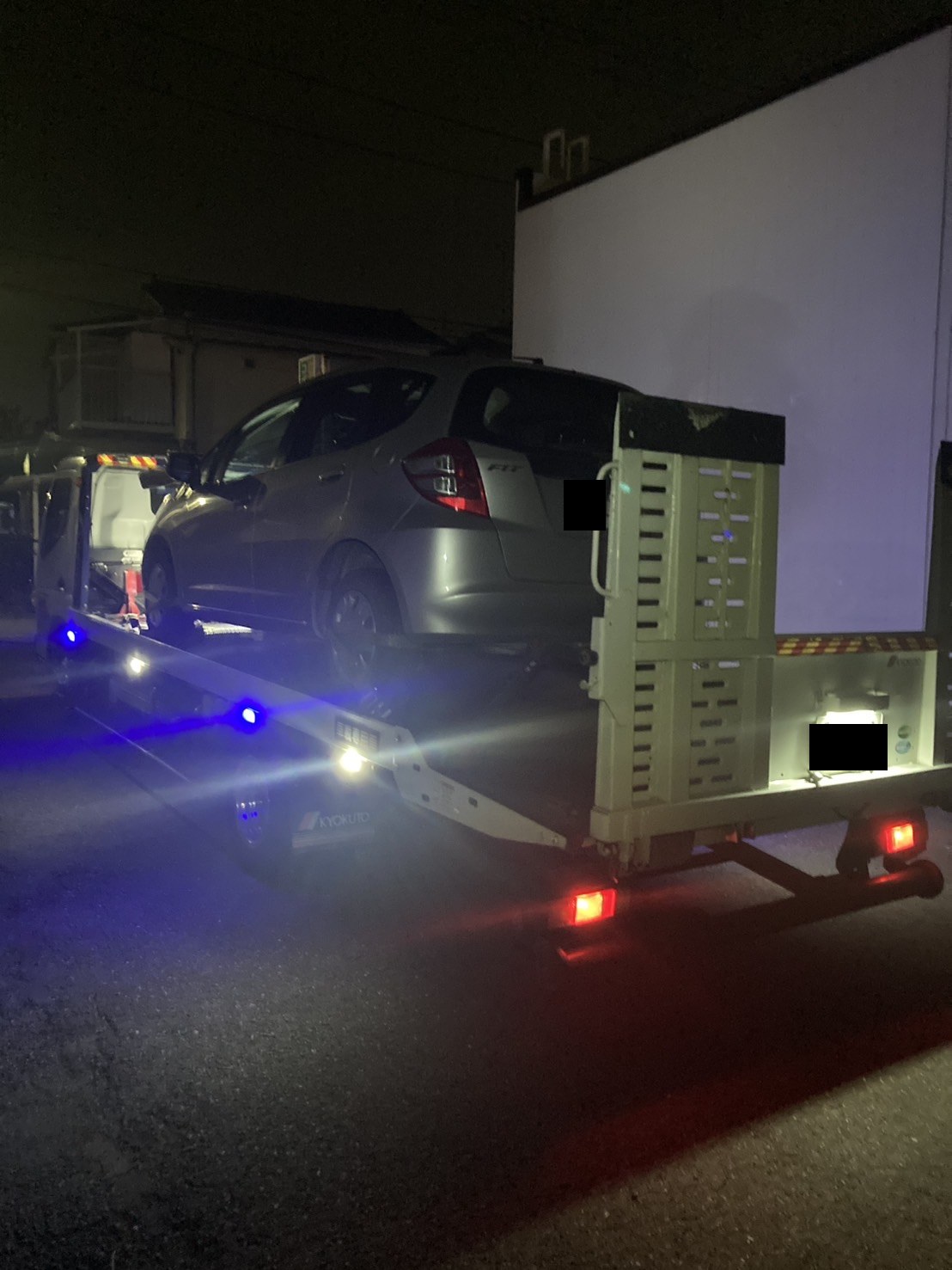 夜間の路上で積載車に車両を載せ終えた様子（ナンバープレートはマスク処理）