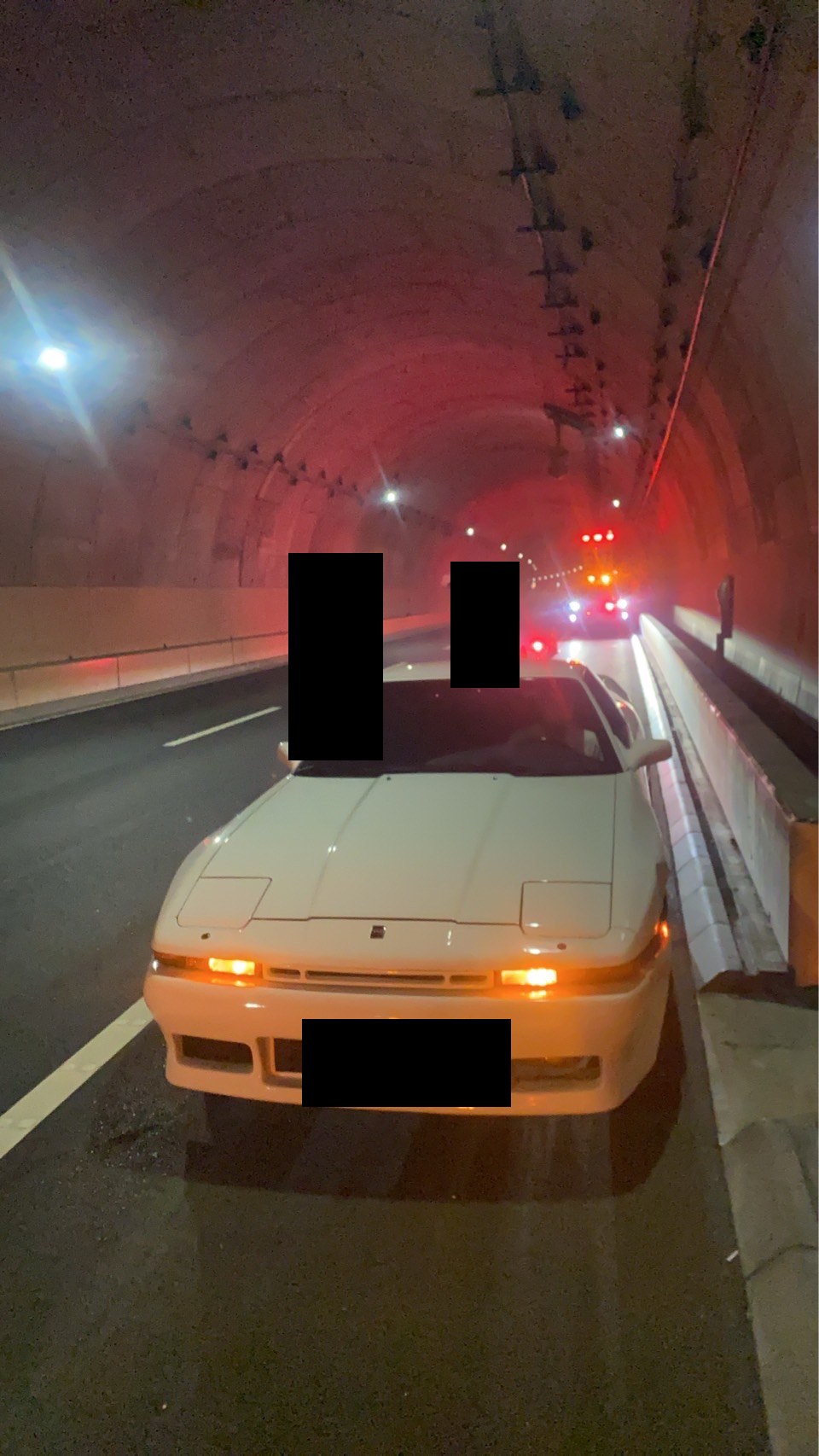 高速道路のトンネル内で路肩に停車した白いスポーツカー（ナンバープレートと現場の作業員はマスク処理）