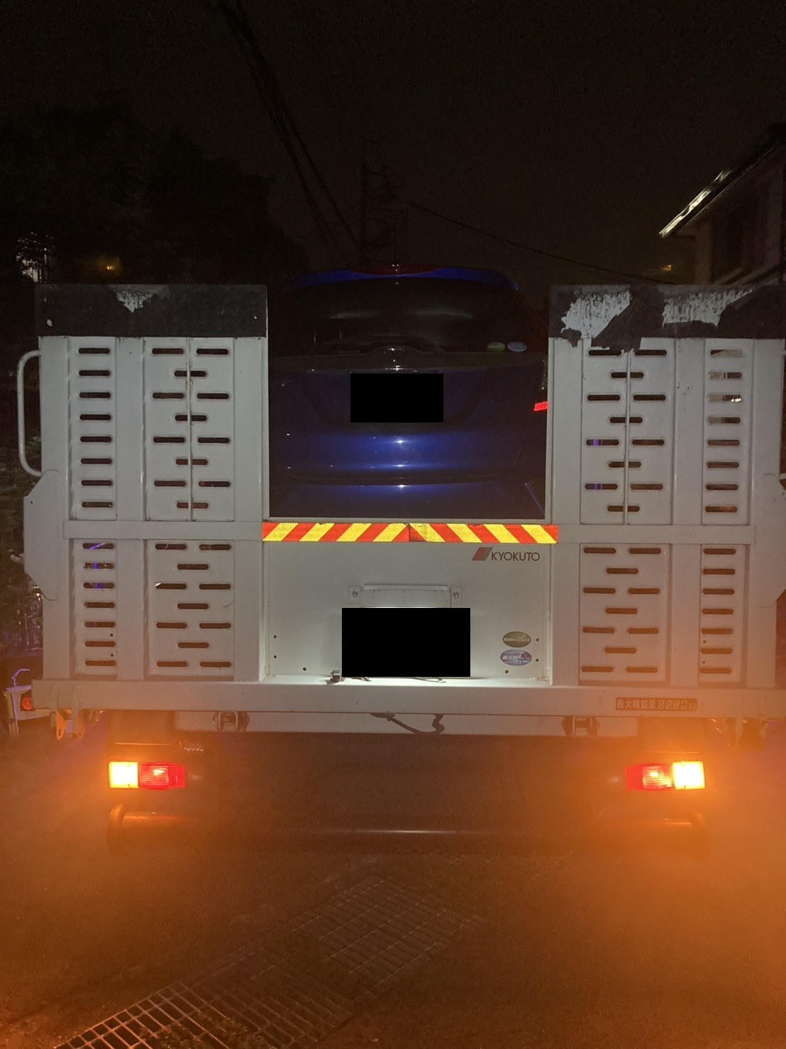 積載車の荷台に固定されたコンパクトカーを後方から見た様子（ナンバープレートはマスク処理）