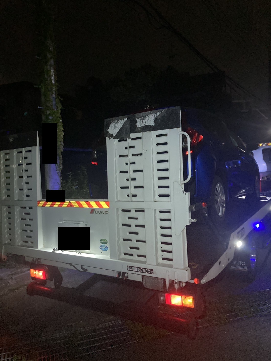 夜間の路上で積載車に車両を載せ終えた様子（ナンバープレートはマスク処理）