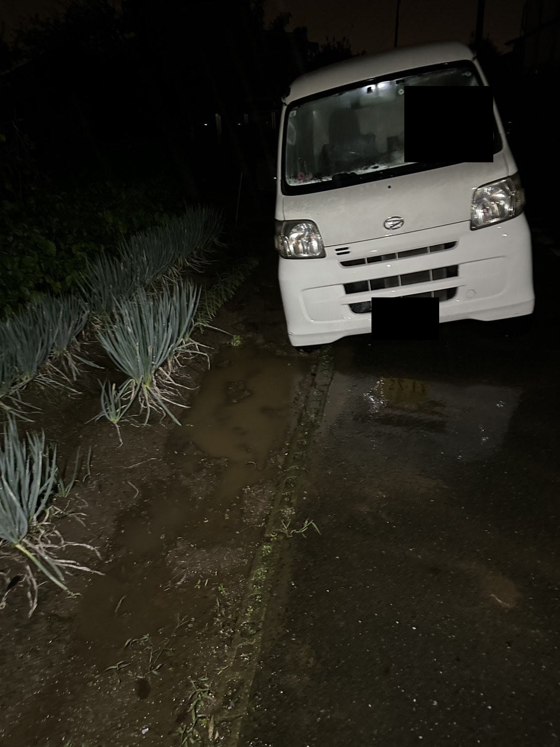 夜間、道路脇のやわらかい路肩に右側のタイヤが落ちて傾いた軽バン（ナンバープレートと車内はマスク処理）