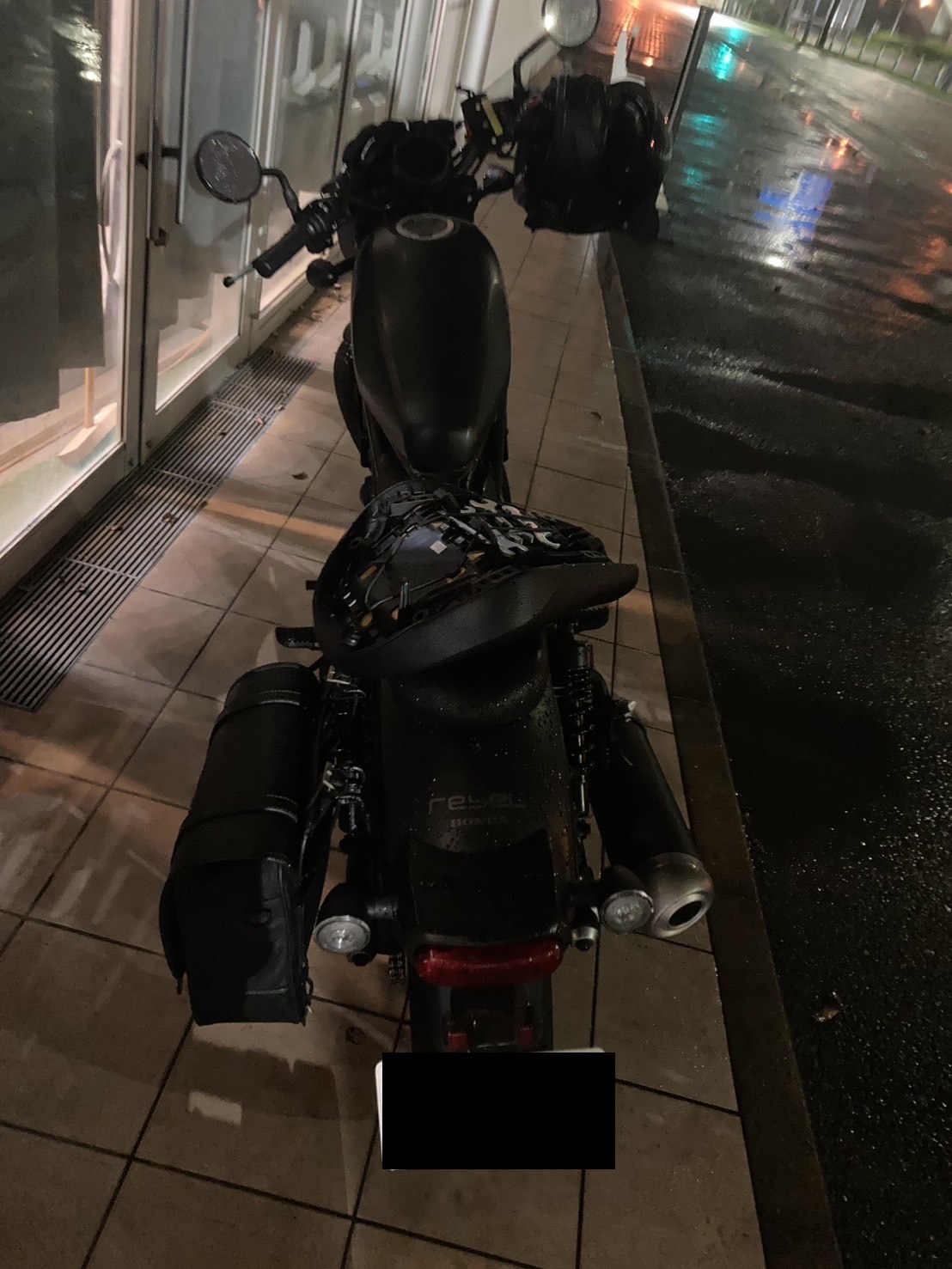 雨の夜、歩道脇に停まったバイクを後方から見た様子（ナンバープレートはマスク処理）