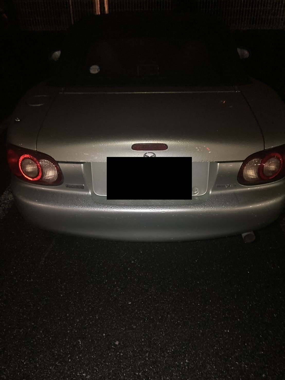 夜間、駐車場に停車した銀色のオープンカーを後方から見た様子（ナンバープレートはマスク処理）