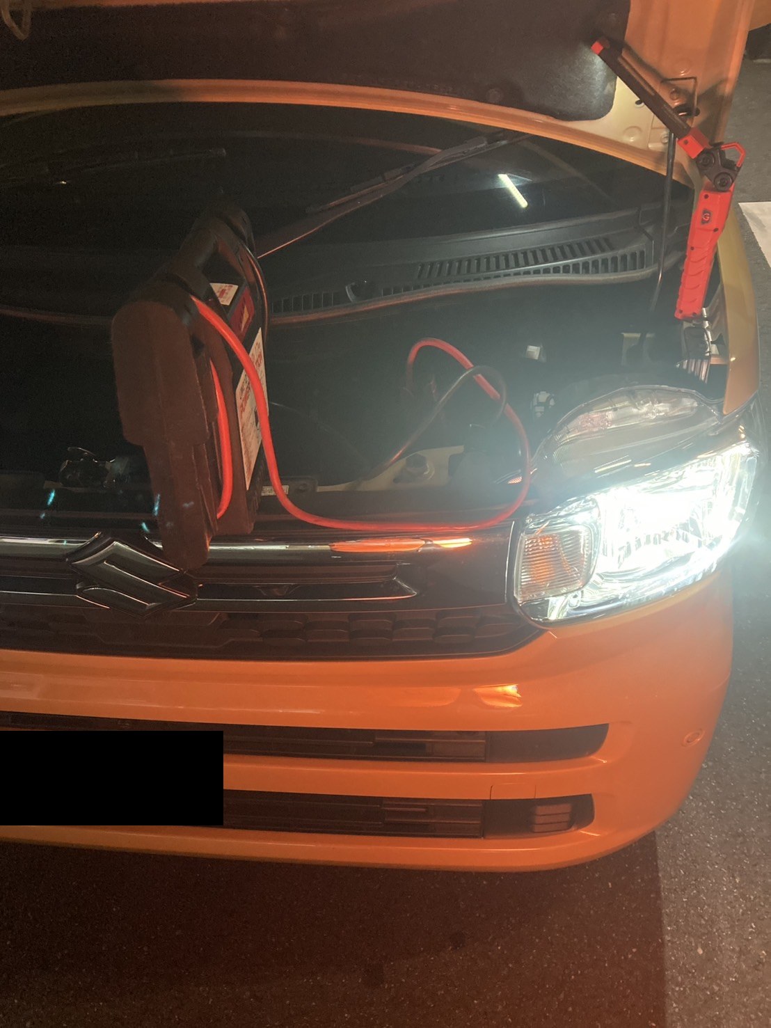ボンネットを開け、ジャンプスターターをつないで始動している軽自動車（ナンバープレートはマスク処理）