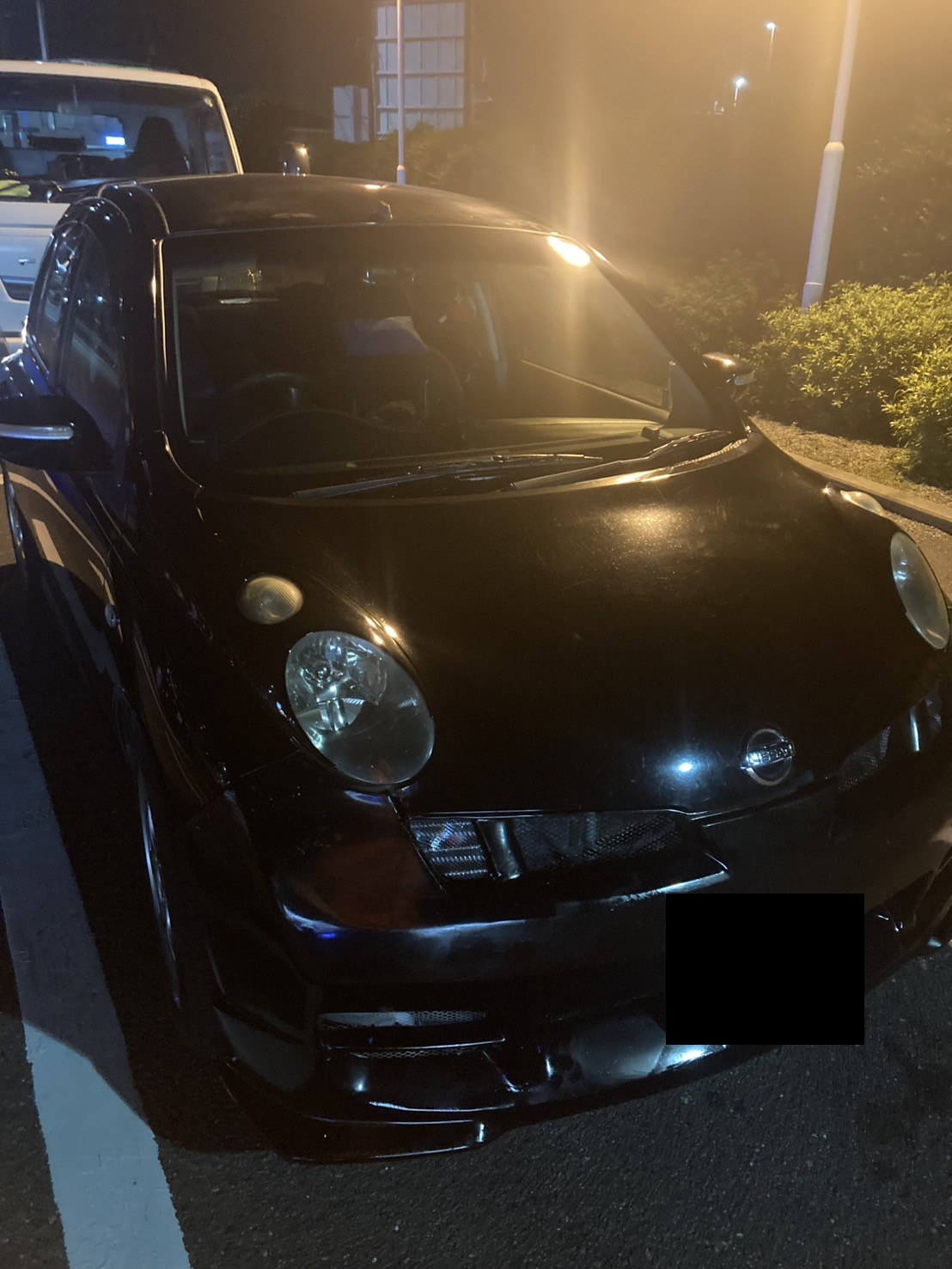 夜間、駐車場に停車した黒いコンパクトカーを前方から見た様子（ナンバープレートはマスク処理）