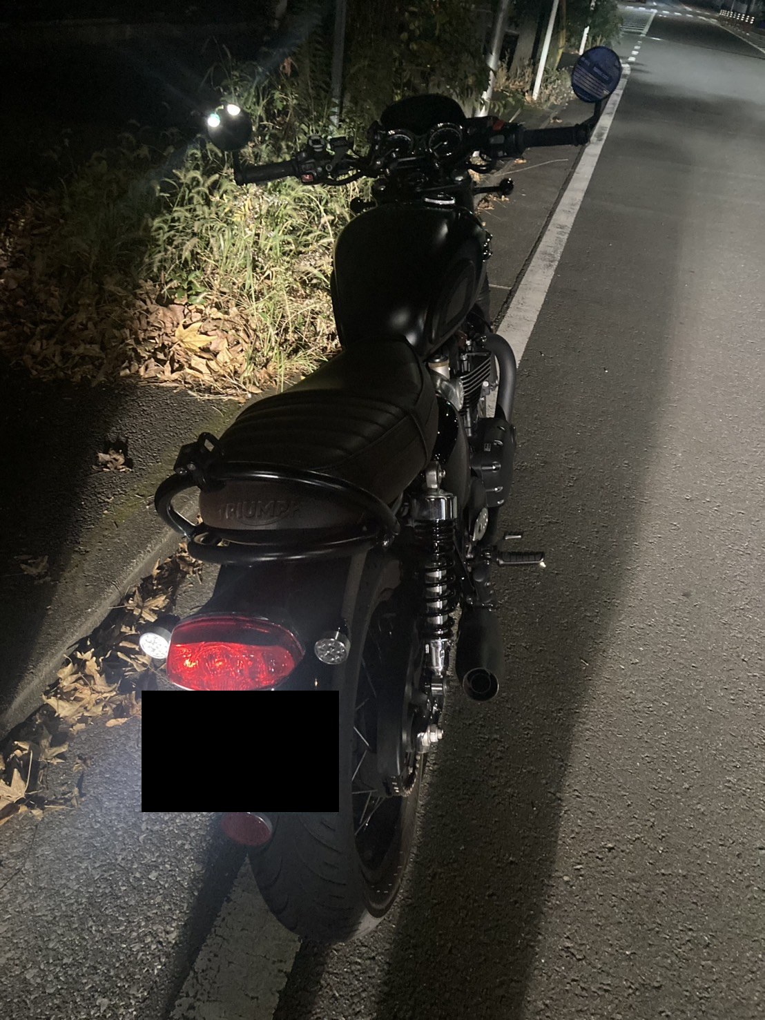 夜間、路肩に停めたクラシックスタイルのバイクを後方から見た様子（ナンバープレートはマスク処理）