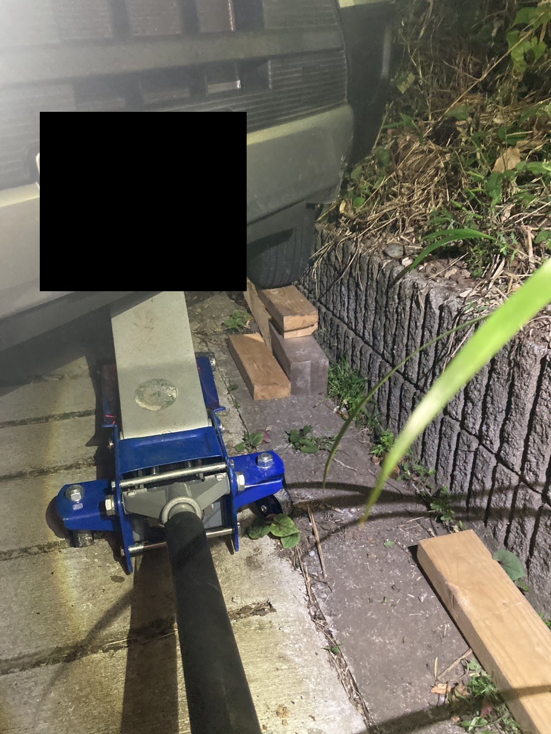 車体の下にジャッキを入れ、タイヤの下に角材を敷いて作業している様子（ナンバープレートはマスク処理）
